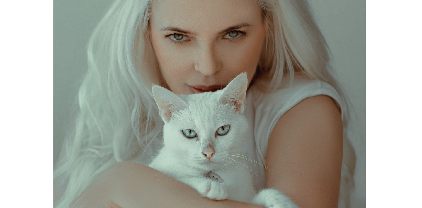 A woman with platinum blonde hair gently holding a white cat with striking blue eyes.